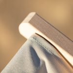 A wooden armrest supports a grey fabric chair, showcasing its design and material texture against a blurred background.