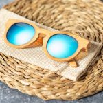 Bamboo sunglasses with blue mirrored lenses resting on a textured beige surface.