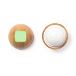 A round lip balm in a natural textured container with a green square. The balm is white and has a logo on the base.