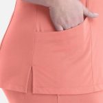 A close-up of a coral women's curved V-neck top featuring a side slit and a pocket.