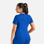 A blue women's curved V-neck top displayed on a model from a side angle, featuring a logo on the back.