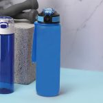 A drink bottle in vibrant blue with a black lid and a strap, positioned beside another blue bottle.