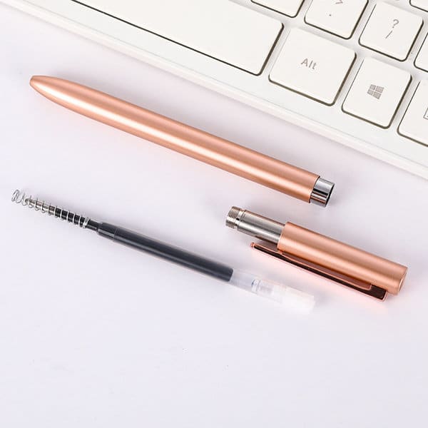 A rose gold custom writing pen displayed alongside its components, resting on a white surface next to a keyboard. A rose gold custom writing pen displayed alongside its components, resting on a white surface next to a keyboard.