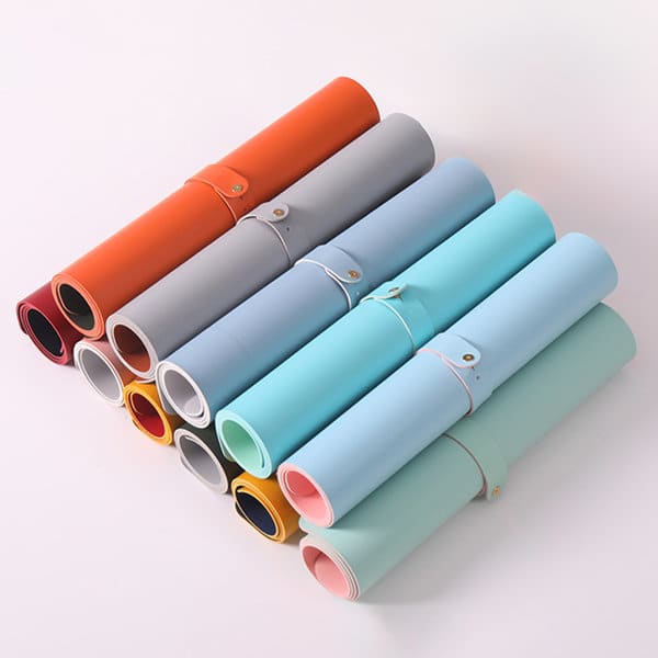 Multiple rolled desk mats in various colours, including grey, orange, blue, and mint, secured with bands. Multiple rolled desk mats in various colours, including grey, orange, blue, and mint, secured with bands.