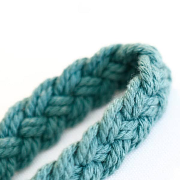 A braided, teal macrame wrist strap, showcasing a textured design and soft, durable fibres. It features a logo. A braided, teal macrame wrist strap, showcasing a textured design and soft, durable fibres. It features a logo.