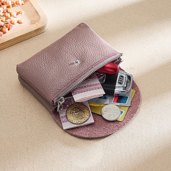 A small leather coin purse in mauve, containing coins, cards, and a key, placed on a textured surface. A small leather coin purse in mauve, containing coins, cards, and a key, placed on a textured surface.