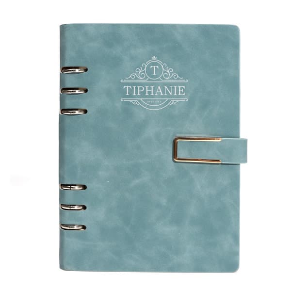 A turquoise PU leather spiral notebook with a buckle and a decorative logo on the cover. A turquoise PU leather spiral notebook with a buckle and a decorative logo on the cover.