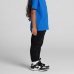 Black kids' track pants paired with a blue t-shirt, featuring a logo on the pants and worn with black sneakers.