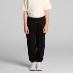 Black youth track pants displayed on a child, paired with a light-coloured t-shirt and casual shoes. It features an elastic waistband.