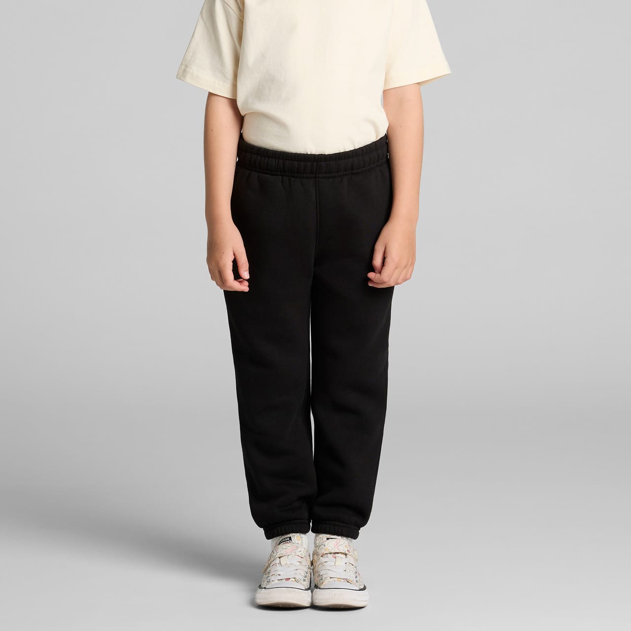 Black youth track pants displayed on a child, paired with a light-coloured t-shirt and casual shoes. It features an elastic waistband. Black youth track pants displayed on a child, paired with a light-coloured t-shirt and casual shoes. It features an elastic waistband.