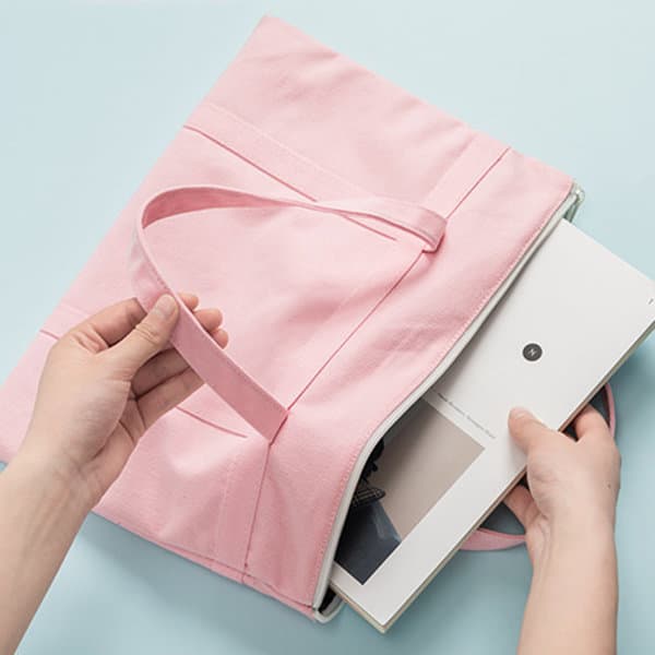 A pink multilayered canvas file bag with a handle, open to reveal a document inside. Features branding. A pink multilayered canvas file bag with a handle, open to reveal a document inside. Features branding.