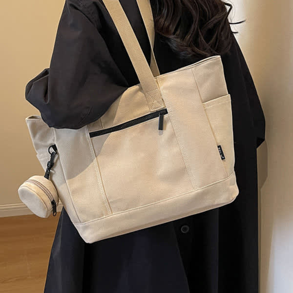 A large capacity canvas shoulder bag in cream, featuring a black zip pocket and a detachable drink bottle holder. A large capacity canvas shoulder bag in cream, featuring a black zip pocket and a detachable drink bottle holder.