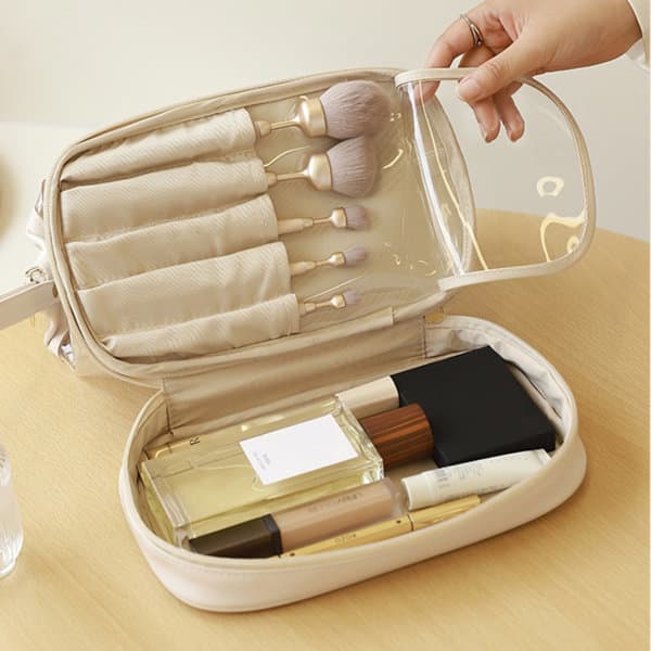 A transparent, double-layered cosmetic toiletry bag in beige, filled with makeup brushes and beauty products. A transparent, double-layered cosmetic toiletry bag in beige, filled with makeup brushes and beauty products.