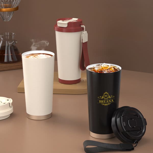 Two stainless steel coffee cups are displayed: one white with a beige base and a red lid, and one black with a gold logo and a black lid. Two stainless steel coffee cups are displayed: one white with a beige base and a red lid, and one black with a gold logo and a black lid.