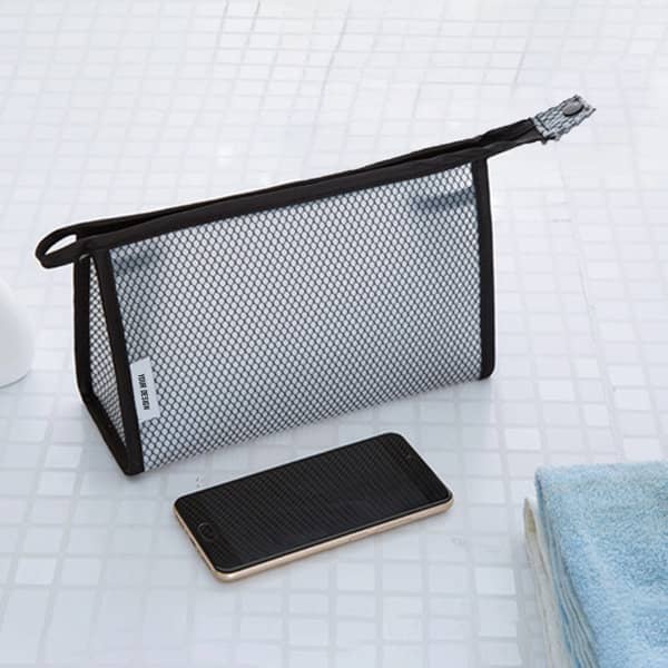 A clear, black mesh makeup bag with a zip top, resting next to a smartphone on a white tiled surface. A clear, black mesh makeup bag with a zip top, resting next to a smartphone on a white tiled surface.