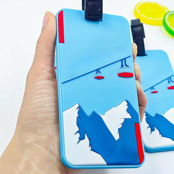 A soft PVC luggage tag in light blue with a mountain and cable car design, featuring a black clip. A soft PVC luggage tag in light blue with a mountain and cable car design, featuring a black clip.