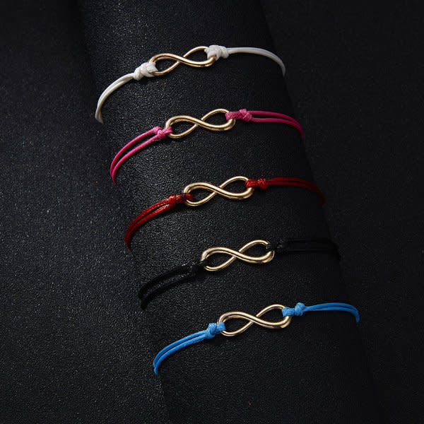 A set of braided infinity-shaped bracelets in white, pink, red, black, and blue, featuring gold-coloured symbols. A set of braided infinity-shaped bracelets in white, pink, red, black, and blue, featuring gold-coloured symbols.