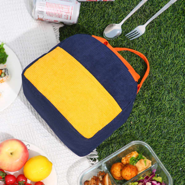 A corduroy insulated lunch bag in navy blue and yellow with an orange zipper, placed on grass beside food items. A corduroy insulated lunch bag in navy blue and yellow with an orange zipper, placed on grass beside food items.