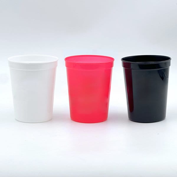Three reusable plastic cups in white, pink, and black, all featuring a simple design and a logo. Three reusable plastic cups in white, pink, and black, all featuring a simple design and a logo.