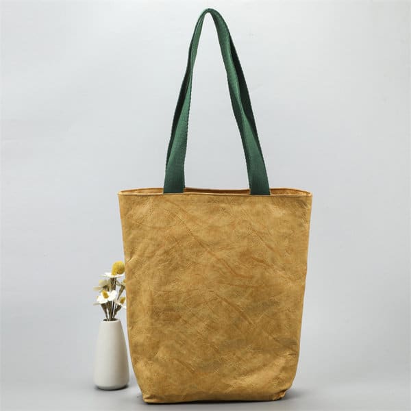 A golden-brown tote bag with green handles, featuring a minimalist design and no visible branding. A golden-brown tote bag with green handles, featuring a minimalist design and no visible branding.