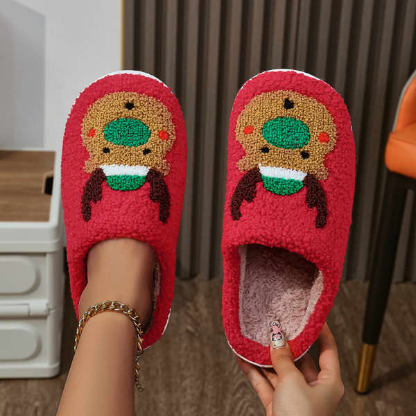 Red fuzzy slippers featuring a reindeer design with green and brown accents, displayed with a person's hands. Red fuzzy slippers featuring a reindeer design with green and brown accents, displayed with a person's hands.