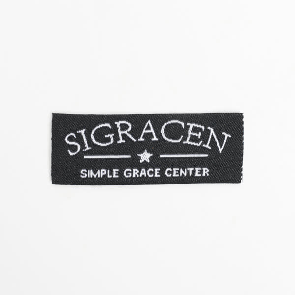 A black woven sewing label featuring white embroidered text and a star design. A black woven sewing label featuring white embroidered text and a star design.