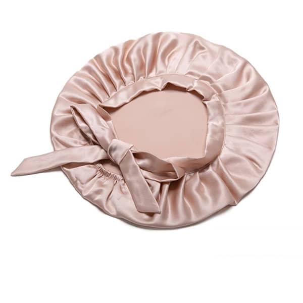 A custom silk bonnet in soft pink, featuring a gathered edge and a satin ribbon tie. It has a logo. A custom silk bonnet in soft pink, featuring a gathered edge and a satin ribbon tie. It has a logo.