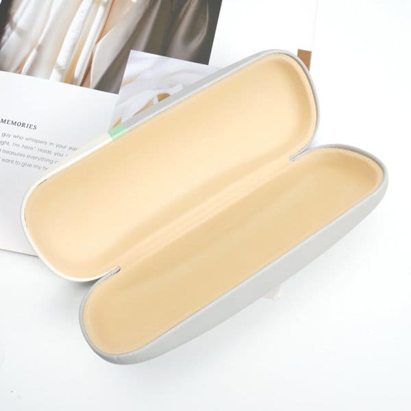A hard-shell sunglasses case in grey with a cream interior, featuring a smooth, sleek design and a logo. A hard-shell sunglasses case in grey with a cream interior, featuring a smooth, sleek design and a logo.