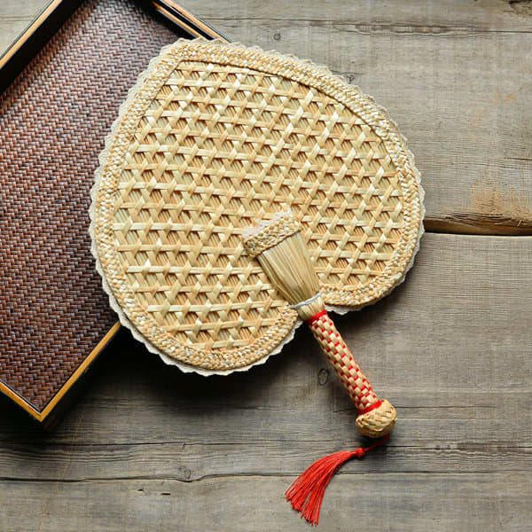 A heart-shaped woven fan made of natural wheat straw, featuring a decorative handle with red accents. A heart-shaped woven fan made of natural wheat straw, featuring a decorative handle with red accents.