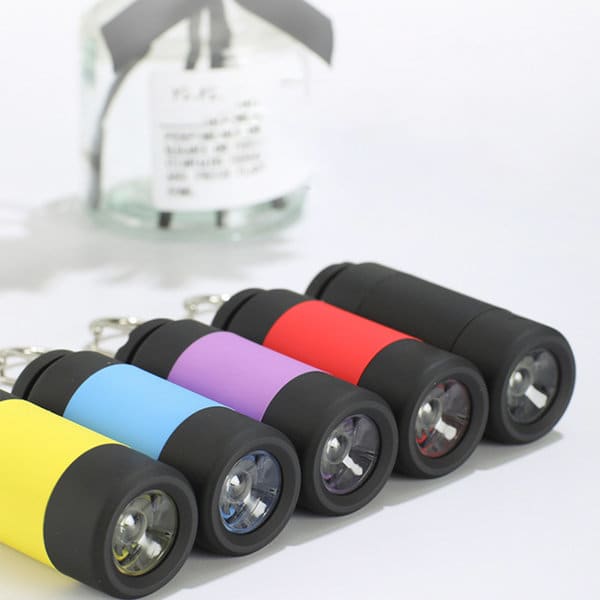 Five LED rechargeable flashlight keychains in yellow, blue, purple, red, and black, with a jar in the background. Five LED rechargeable flashlight keychains in yellow, blue, purple, red, and black, with a jar in the background.