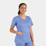 A woman in a light blue double V-neck top with a pocket, smiling against a plain background.
