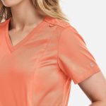 A women's double V-neck top in coral, featuring short sleeves and a subtle shoulder detail. It has a logo.