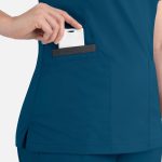A women's double V-neck top in teal, featuring a side pocket with a card being inserted. It has a discreet logo.