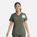 A nurse in an olive green double V-neck top with a dark trim, featuring a badge and logo.