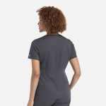 A woman with curly hair wearing a grey tuckable V-neck top, viewed from the back. The top has a logo on the sleeve.