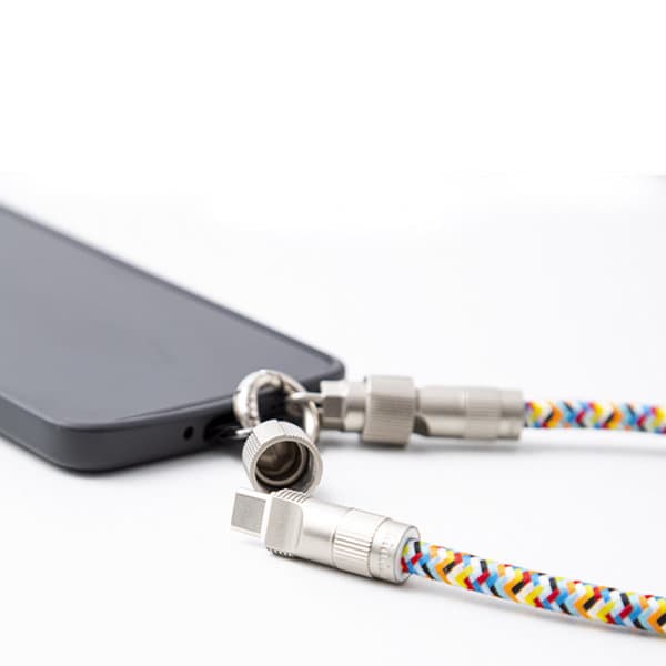 A multi-functional charging cable with a colourful braided design, featuring metal connectors, attached to a smartphone. A multi-functional charging cable with a colourful braided design, featuring metal connectors, attached to a smartphone.