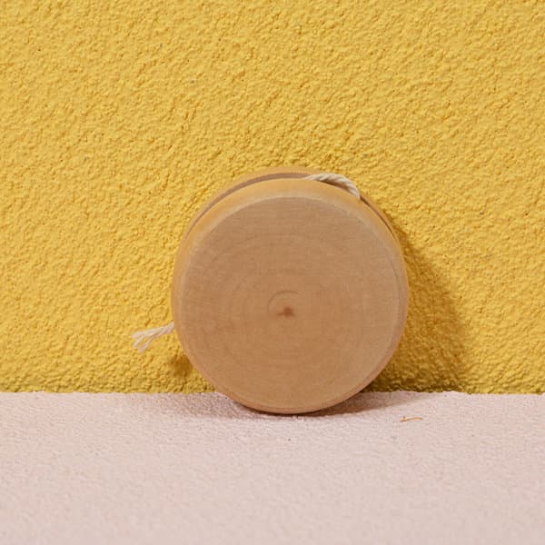 A natural wooden yoyo sits against a yellow wall, showcasing its smooth, circular design. A natural wooden yoyo sits against a yellow wall, showcasing its smooth, circular design.
