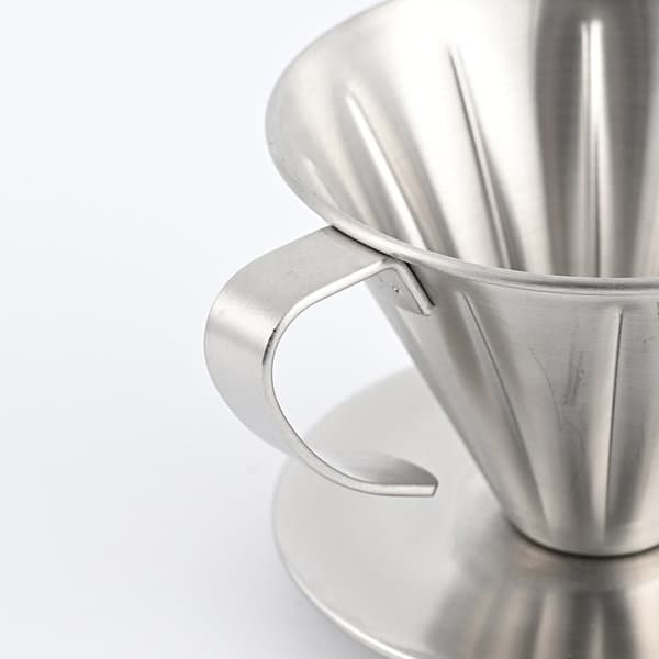 A stainless steel coffee dripper with a handle and a matching base, featuring a shiny, metallic finish. A stainless steel coffee dripper with a handle and a matching base, featuring a shiny, metallic finish.