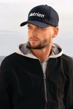A navy blue cap with a logo, worn by a man in a black jacket and grey hoodie.
