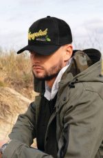 A black cap with a mesh back and a logo featuring the word "Recycled," worn by a person in an outdoor setting.