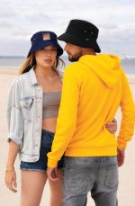 A black and blue bucket hat displayed on a sandy beach, worn by two individuals, one in a yellow hoodie.