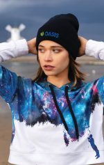 A black beanie with a logo paired with a colourful galaxy-themed hoodie, worn by a model outdoors.