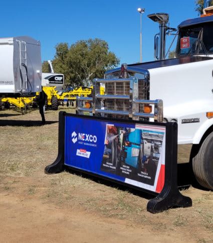 A signage barrier featuring a branded design, predominantly blue and red, displayed in an outdoor setting near equipment. Signage Barrier 3m Single Sided - Image 1