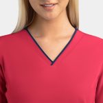 A close-up of a women's pink V-neck top featuring a navy blue contrast trim and a logo.