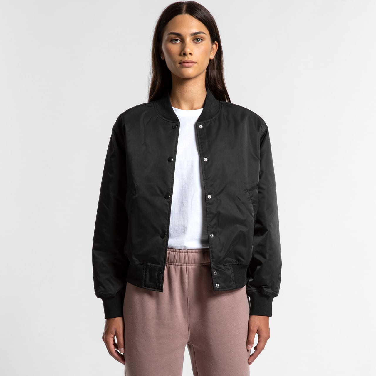 A black bomber jacket featuring a front snap closure, worn over a white shirt and light-coloured pants. A black bomber jacket featuring a front snap closure, worn over a white shirt and light-coloured pants.