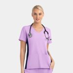A mock wrap top in lilac with contrast navy panels, featuring short sleeves and pockets, worn by a model with a stethoscope.