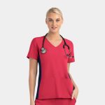 A bright pink women's mock wrap top with contrast navy panels, featuring two front pockets and a stethoscope.