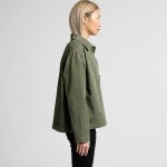A side view of a green chore jacket with a relaxed fit and a chest pocket. The model is wearing black pants.