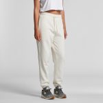 Track pants in cream colour with an elastic waistband and pockets, paired with grey sneakers. Features a logo.