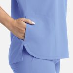 A light blue women's top featuring a dolman sleeve design and three pockets. It has a logo on it.